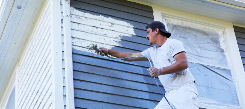 painter using a spray paint gun to paint the exterior of a home